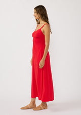 [Color: Tomato] A side facing image of a brunette model wearing a classic red maxi dress. This linen blend maxi features a button front, side pockets, and a smocked back.