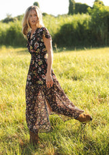 [Color: Black/Rust] A side facing image of a black floral maxi dress with short flutter sleeves, a split v-neckline, a smocked waist, and side slit. Adorned with ruffle trims, this romantic fall maxi dress is perfect for weddings, holidays, and other special occasions. 