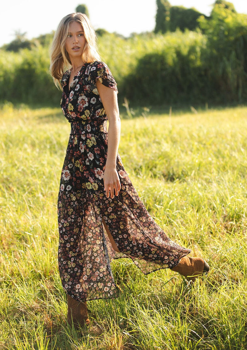 [Color: Black/Rust] A side facing image of a black floral maxi dress with short flutter sleeves, a split v-neckline, a smocked waist, and side slit. Adorned with ruffle trims, this romantic fall maxi dress is perfect for weddings, holidays, and other special occasions. 