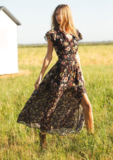 [Color: Black/Rust] A front facing image of a black floral maxi dress with short flutter sleeves, a split v-neckline, a smocked waist, and side slit. Adorned with ruffle trims, this romantic fall maxi dress is perfect for weddings, holidays, and other special occasions. 
