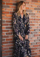 [Color: Navy/Yellow] A front facing image of a blonde model wearing a navy floral maxi dress with long sleeves, a smocked waist, and a split v-neckline. A classic floral maxi for weddings and special occasions. 