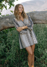 [Color: Natural/Navy] A front facing image of a blonde model wearing a striped floral pattern mini dress with long sleeves, a surplice v-neckline, and an elastic waist with tie detail. A casual fall boho dress for brunch and special occasions. 
