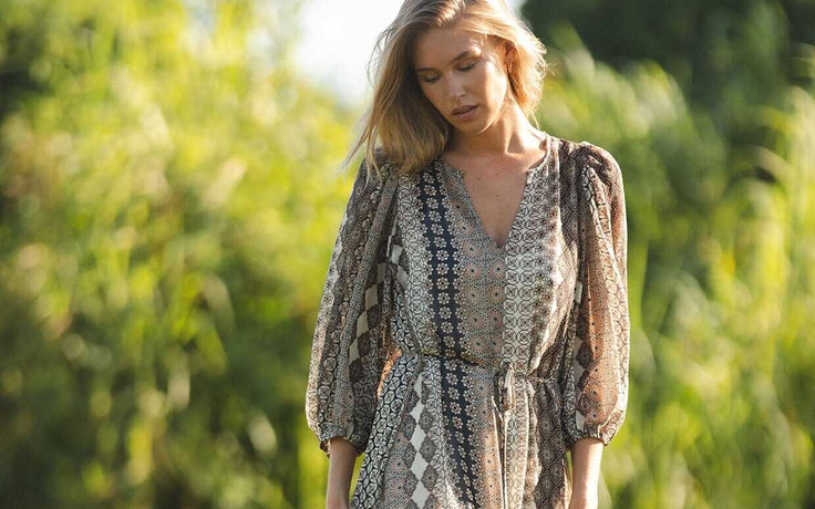 Woman in a patterned dress standing in a natural setting with greenery.
