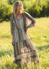 [Color: Natural/Navy] A front facing image of a blonde model wearing boho floral maxi dress with 3/4 volume sleeves, waist belt, and a high low tiered skirt. 