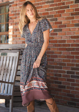 [Color: Navy/Rose] A front facing image of a blonde model wearing a navy floral border print midi dress with a classic v-neckline, short sleeves, a smocked waist, and side pockets. A fall bohemian dress perfect for any occasion. 
