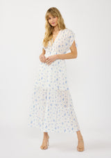 [Color: White/Blue] A front facing image of a blonde model wearing a spring white and blue floral maxi dress with short dolman sleeves, tassel ties, a v neckline, and a smocked waist. 