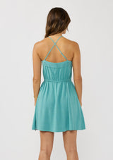 [Color: Teal] A back facing image of a brunette model wearing a teal sleeveless mini dress with spaghetti straps, a cross back, button front, drawstring waist, and side pockets. 