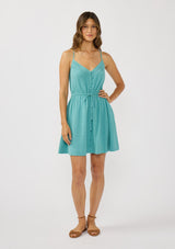 [Color: Teal] A front facing image of a brunette model wearing a teal sleeveless mini dress with spaghetti straps, a cross back, button front, drawstring waist, and side pockets. 