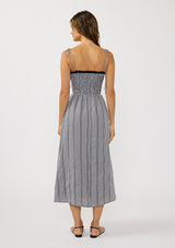 [Color: Black/White] A back facing image of a brunette model wearing a black and white gingham midi dress with a smocked bodice, tie shoulder straps, and side pockets. 