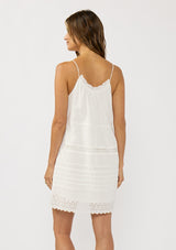 [Color: White] A back facing image of a brunette model wearing a white bohemian sleeveless mini dress with eyelet trims, pintucks, and a ruched neckline with ruffle trims.