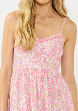 [Color: Natural/Dusty Rose] A detail image of a blonde model wearing a pink floral midi dress with a v neckline, spaghetti straps, a smocked back, and side pockets.