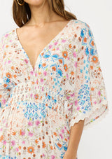 [Color: Ivory/Orange] A detail image of a brunette model wearing a blue and orange kimono sleeve maxi dress with a deep v neckline, smocked waist, tie back detail, and side slits. 