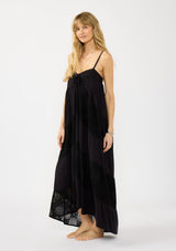 [Color: Black] A side facing image of a blonde model wearing a black bohemian maxi dress with a patchwork lace, sweetheart neckline, tie front detail, and a flowy tiered silhouette. 
