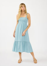 [Color: Aqua Blue] A front facing image of a blonde model wearing a light blue midi dress with a smocked bust, button front, and ruffle tiered  hemline. 