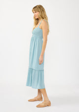 [Color: Aqua Blue] A side facing image of a blonde model wearing a light blue midi dress with a smocked bust, button front, and ruffle tiered  hemline. 