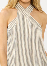 [Color Natural/Black] A detail image of a blonde model wearing a striped halter maxi dress with a crossover neckline, single pleat, and side pockets. 