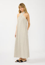 [Color Natural/Black] A side facing image of a blonde model wearing a striped halter maxi dress with a crossover neckline, single pleat, and side pockets.