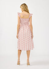[Color: Paprika/White] A back facing image of a blonde model wearing a red floral midi dress with eyelets. Featuring a smocked bust, elastic straps with ruffle detail, and a tie back detail.