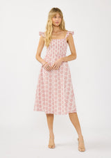 [Color: Paprika/White] A front facing image of a blonde model wearing a red floral midi dress with eyelets. Featuring a smocked bust, elastic straps with ruffle detail, and a tie back detail.