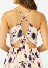 [Color: Peach/Plum] A back facing image of a brunette model wearing a pink and purple floral maxi dress with a pleated design, v neckline, spaghetti straps, and a cross back with tie back detail. 