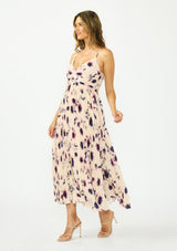 [Color: Peach/Plum] A side facing image of a brunette model wearing a pink and purple floral maxi dress with a pleated design, v neckline, spaghetti straps, and a cross back with tie back detail. 