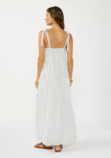 [Color: White/Denim Blue] A back facing image of a brunette model wearing a white and blue striped maxi dress with a shirred texture, square neckline, and tie shoulders. 