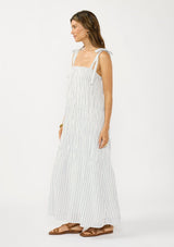 [Color: White/Denim Blue] A side facing image of a brunette model wearing a white and blue striped maxi dress with a shirred texture, square neckline, and tie shoulders. 