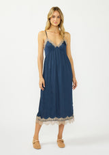 [Color: Navy/Taupe] A front facing image of a blonde model wearing a navy blue lace midi dress with spaghetti straps and an empire waist. 