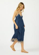 [Color: Navy/Taupe] A side facing image of a blonde model wearing a navy blue lace midi dress with spaghetti straps and an empire waist. 