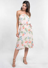 [Color: Blush/Green] A front facing image of a woman modeling a strapless top and matching midi skirt set with a pink and green tropical floral print paired with beige strappy high-heeled sandals.