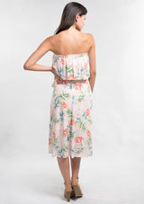 [Color: Blush/Green] A back facing image of a woman modeling a strapless top and matching midi skirt set with a pink and green tropical floral print paired with beige strappy high-heeled sandals.