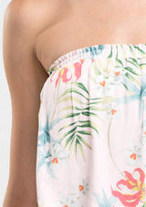 [Color: Blush/Green] A detail image of a woman modeling a strapless top and matching midi skirt set with a pink and green tropical floral print paired with beige strappy high-heeled sandals.