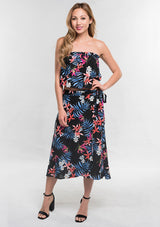 [Color: Black/Coral] A front facing image of a woman modeling a strapless top and matching midi skirt set with a black and blue tropical floral print paired with black block heels.