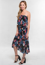 [Color: Black/Coral] A side facing image of a woman modeling a strapless top and matching midi skirt set with a black and blue tropical floral print paired with black block heels.