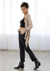 [Color: Pale Mauve] A side facing image of a brunette model wearing a pointelle knit cardigan with metallic thread details, a waterfall front, and long cozy sleeves. 