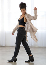 [Color: Pale Mauve] A side facing image of a brunette model wearing a pointelle knit cardigan with metallic thread details, a waterfall front, and long cozy sleeves. 