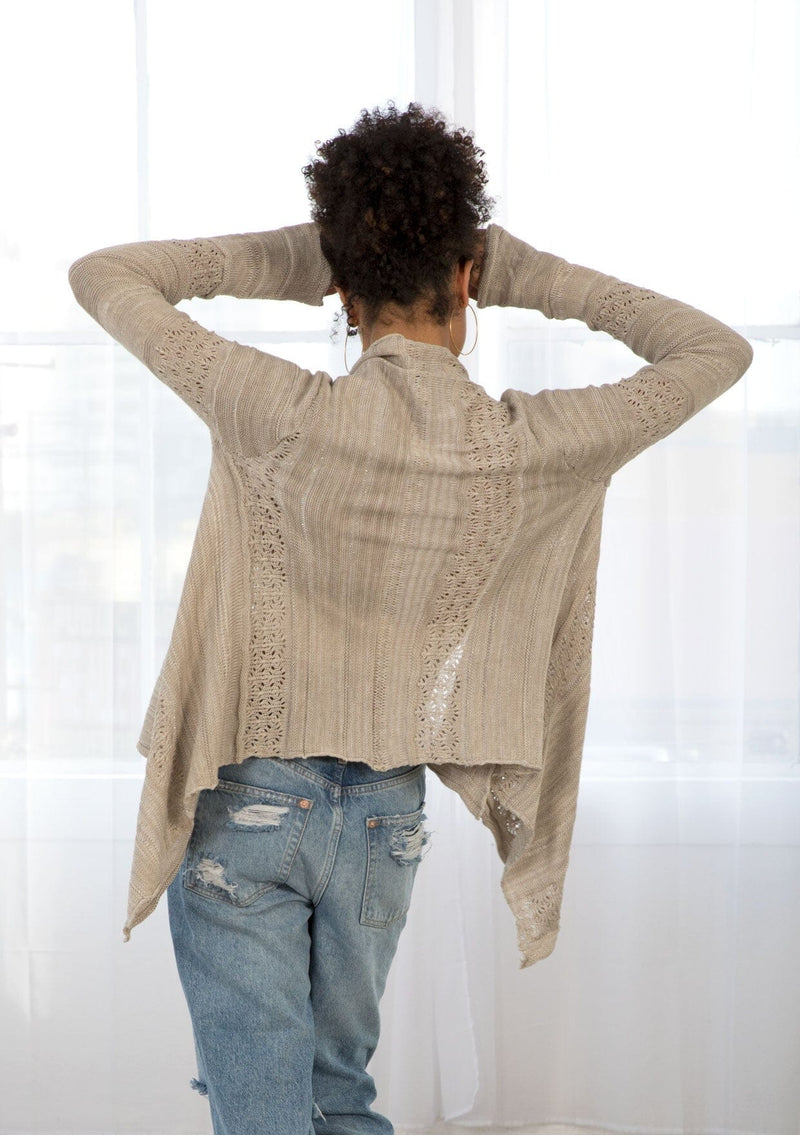 [Color: Warm Grey] A back facing image of a brunette model wearing a pointelle knit cardigan with metallic thread details, a waterfall front, and long cozy sleeves. 