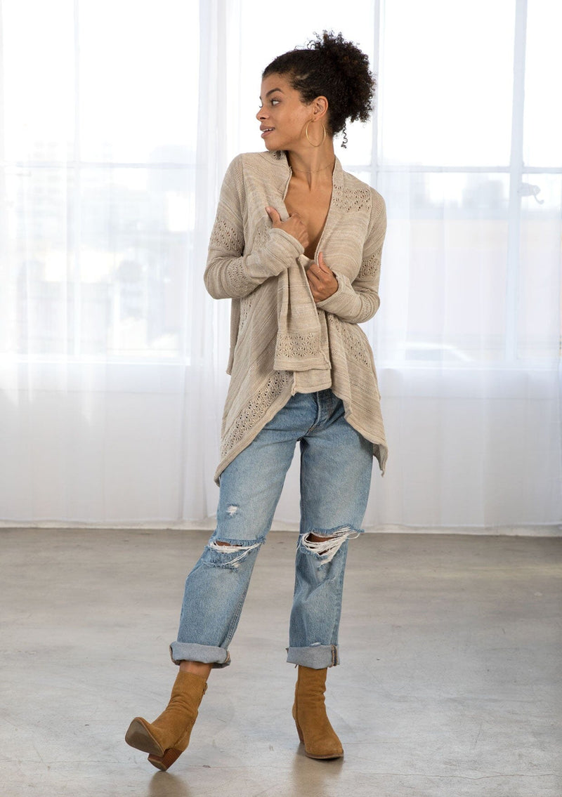 [Color: Warm Grey] A front facing image of a brunette model wearing a pointelle knit cardigan with metallic thread details, a waterfall front, and long cozy sleeves. 