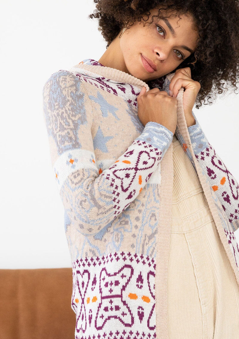 [Color: Sky/Plum] A detail image of a brunette model wearing a vibrant boho patterned knit cardigan with long cozy sleeves, open front, and hoodie. An effortless statement sweater for easy layering.  