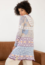 [Color: Sky/Plum] A side facing image of a brunette model wearing a vibrant boho patterned knit cardigan with long cozy sleeves, open front, and hoodie. An effortless statement sweater for easy layering.  