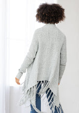 [Color: Grey/Ivory] A back facing image of a marled knit cardigan with a shawl waterfall collar with a fringe hem. A boho chic cardigan for the fall season. 