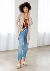 [Color: Mushroom] A front facing image of a brunette model wearing a beige cardigan with a sheer back. Featuring cozy ribbed sleeves, and open front, and shawl collar. A casual fall style for effortless layering. 