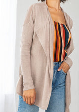 [Color: Mushroom] A detail image of a brunette model wearing a beige cardigan with a sheer back. Featuring cozy ribbed sleeves, and open front, and shawl collar. A casual fall style for effortless layering. 