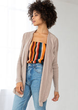 [Color: Mushroom] A front facing image of a brunette model wearing a beige cardigan with a sheer back. Featuring cozy ribbed sleeves, and open front, and shawl collar. A casual fall style for effortless layering. 