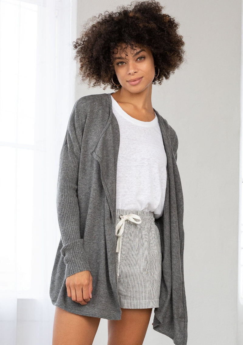 [Color: Dark Grey] A front facing image of a brunette model wearing a grey cardigan with a sheer back. Featuring cozy ribbed sleeves, and open front, and shawl collar. A casual fall style for effortless layering. 
