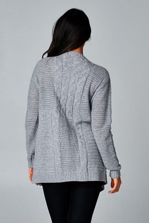 [Color: Grey] A back facing image of a brunette model wearing a cozy grey open knit cardigan with a shawl collar, cable knit details, and ribbed trims. A casual fall cardigan for any occasion. 