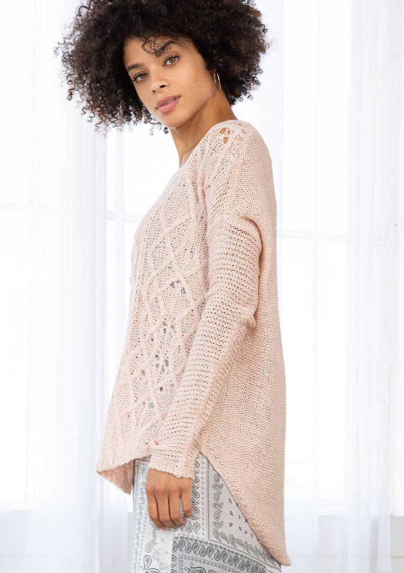 [Color: Blush] A side facing image of a brunette model wearing a lightweight cable knit pullover with open knit details. Featuring a classic round neckline, dropped shoulders, long sleeves, and a shirttail hem. Laid-back boho style for casual outings. 