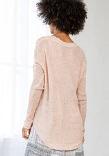 [Color: Blush] A back facing image of a brunette model wearing a lightweight cable knit pullover with open knit details. Featuring a classic round neckline, dropped shoulders, long sleeves, and a shirttail hem. Laid-back boho style for casual outings. 
