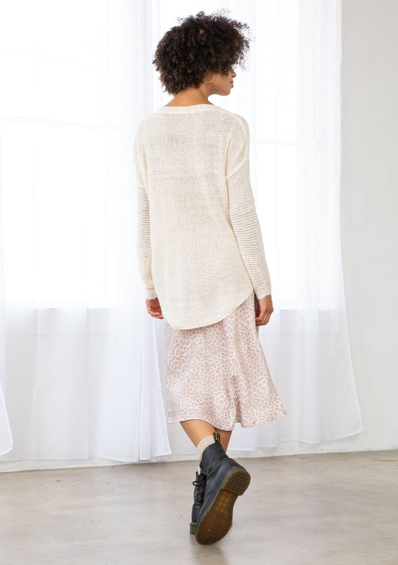 [Color: Vanilla] A back facing image of a brunette model wearing a lightweight cable knit pullover with open knit details. Featuring a classic round neckline, dropped shoulders, long sleeves, and a shirttail hem. Laid-back boho style for casual outings. 