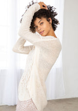 [Color: Vanilla] A side facing image of a brunette model wearing a lightweight cable knit pullover with open knit details. Featuring a classic round neckline, dropped shoulders, long sleeves, and a shirttail hem. Laid-back boho style for casual outings. 